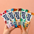 Hand holding a variety of Zing energy bar packages on a peach background